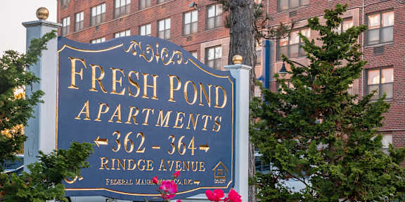 A sign for Fresh Pond Apartments sits in front of a building.