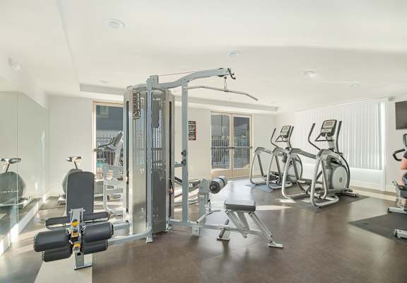 A well-equipped gym with a variety of machines and a person working out on a stationary bike at Woodley Sara Apartment, Van Nuys, 91406