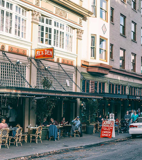 A street view of a restaurant with people sitting at tables outside.