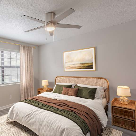 A bedroom with a large bed, a ceiling fan, and a painting on the wall.