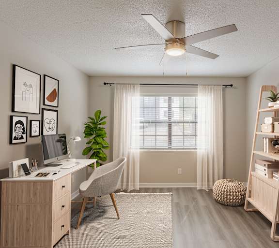 A room with a desk, chair, and a plant.