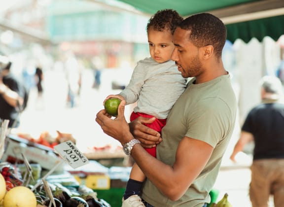 a man holding a child at a market holding an apple