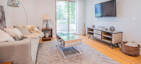 A modern living room with a grey sofa, a glass coffee table, a wooden cabinet, and a flat-screen TV mounted on the wall at Woodley Sara Apartment, Van Nuys, 91406