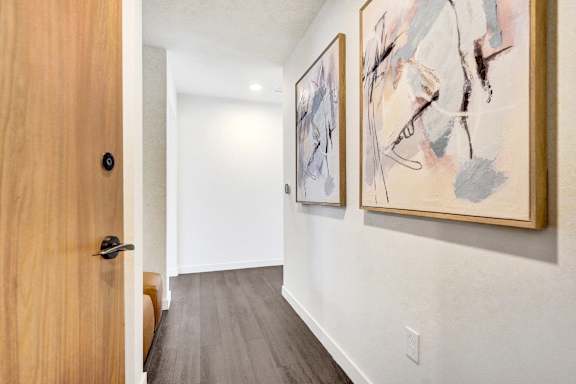 A hallway with a wooden door and two paintings on the wall.