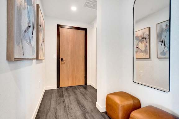 A hallway with a wooden door and two brown ottomans.