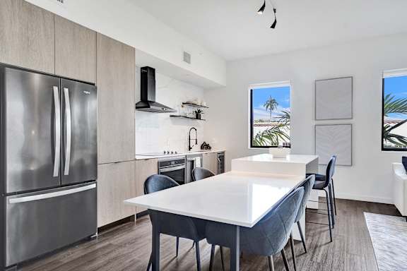 A modern kitchen with a large island and a refrigerator on the left.