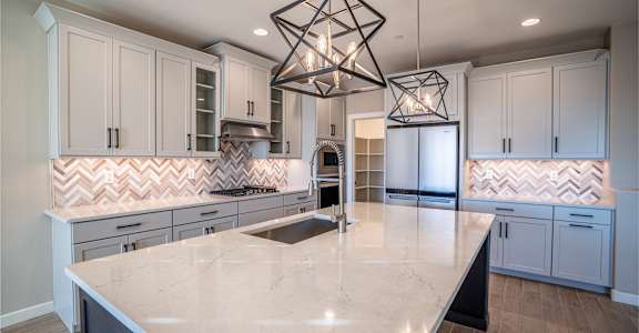 A modern kitchen with a large island and a geometric chandelier.