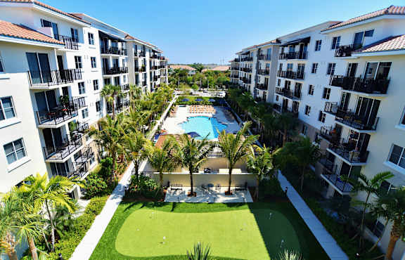 A view of a luxury apartment complex with a pool and palm trees.