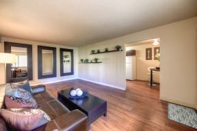 Large Living Room with Hardwood Inspired Floors, Open Windows, Black Sofa, Small Black Table, Mirrors on Wall and View of Kitchen