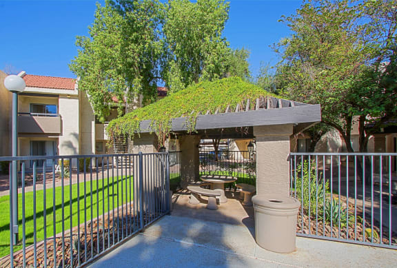 a patio with a gazebo and a fence with a lawn and trees