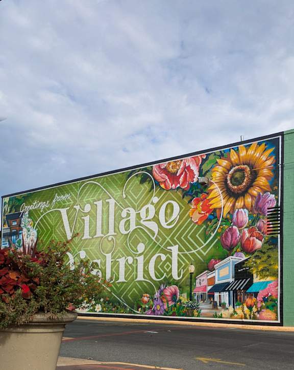A mural on a building wall says "Village District" and is decorated with flowers.