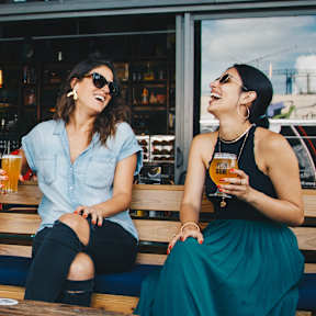 Two women sitting on a bench, one holding a glass of beer.