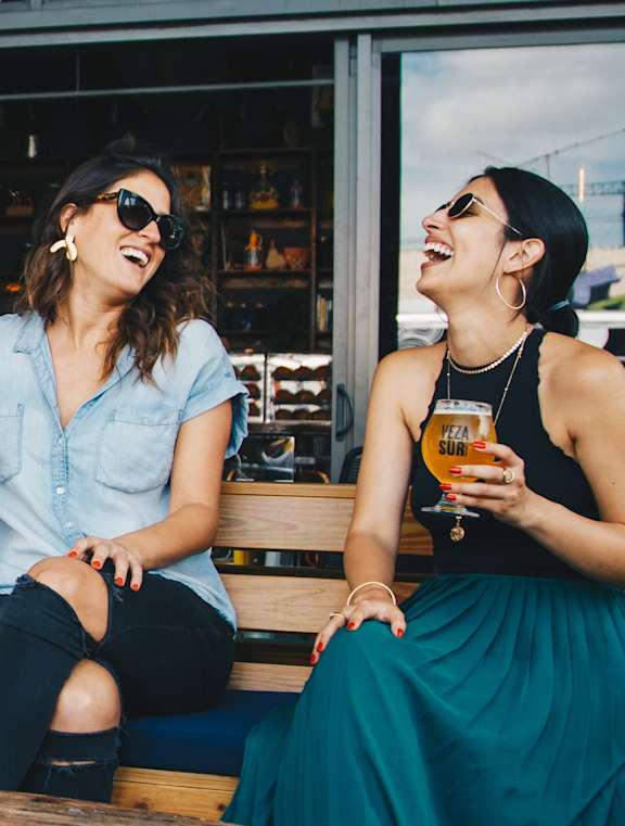 Two women sitting on a bench, one holding a glass of beer.