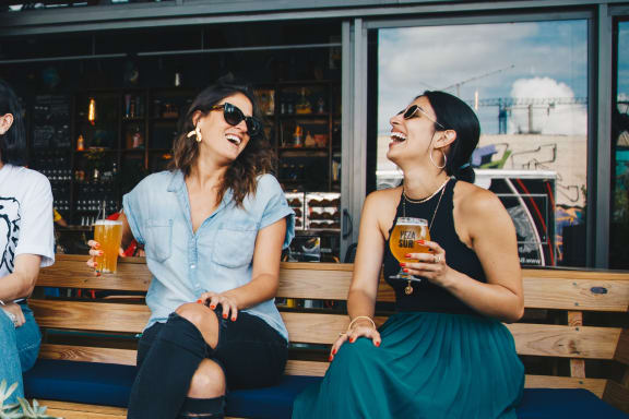 two women sitting on a bench drinking beer