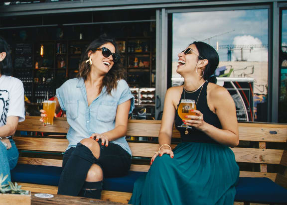 two women sitting on a bench laughing and drinking beer