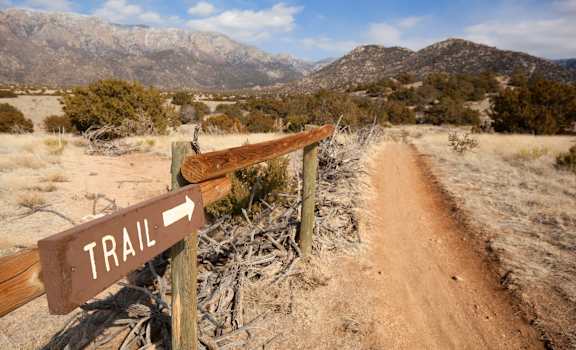 a trail sign next to a dirt road in the desert