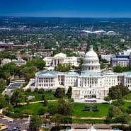 The image showcases a large, white, neoclassical building with a dome, surrounded by greenery and a clear blue sky.