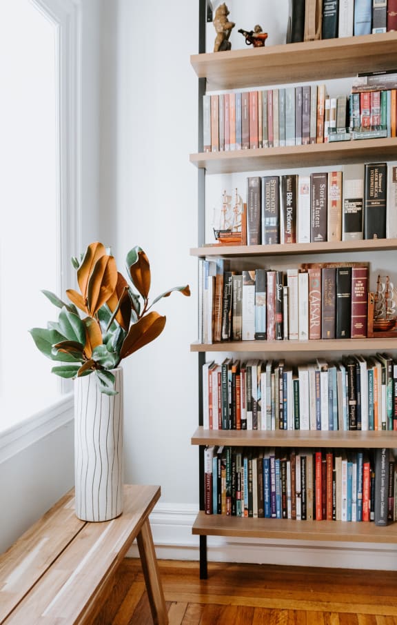 a bookcase filled with books next to a wooden bench with a vase of flowers