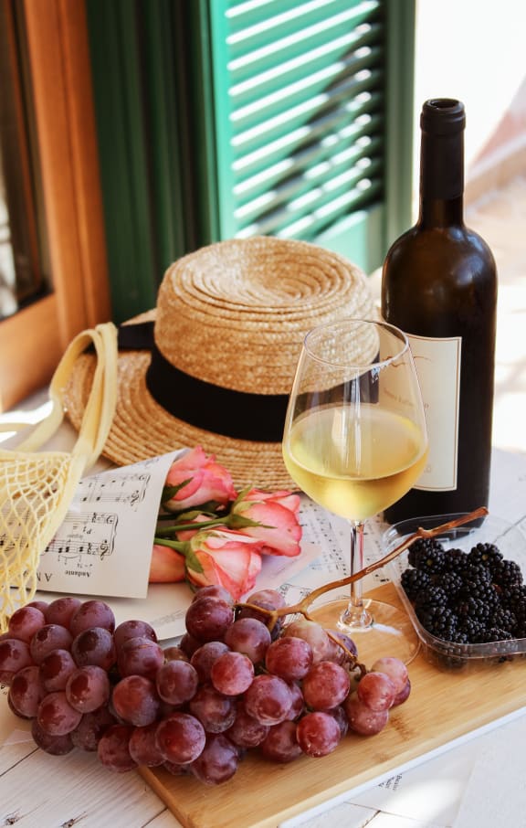 a bottle of wine and a glass of wine on a table with grapes and a straw hat