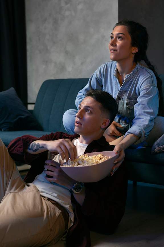 A man and woman sitting on a couch with a bowl of popcorn in front of them at Beton Apartments, Wembley, HA9 0SL