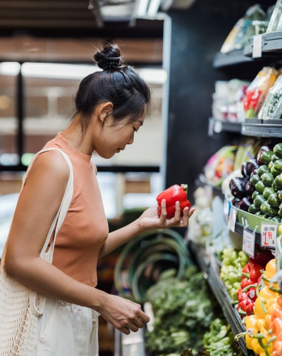 a woman is looking at a bell pepper in the produce section of a grocery store