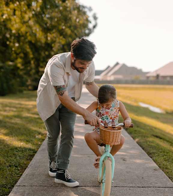 A man is teaching a little girl how to ride a bike.