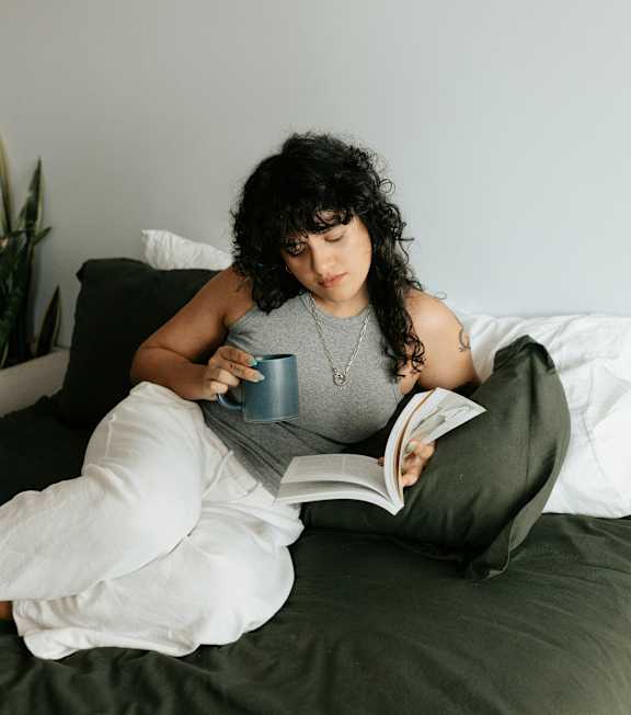 A woman is reading a book while sitting on a bed.