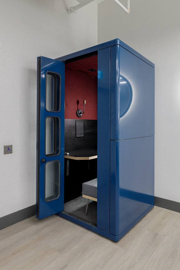 A blue pod-like structure with a door open to reveal a black interior with a bench.