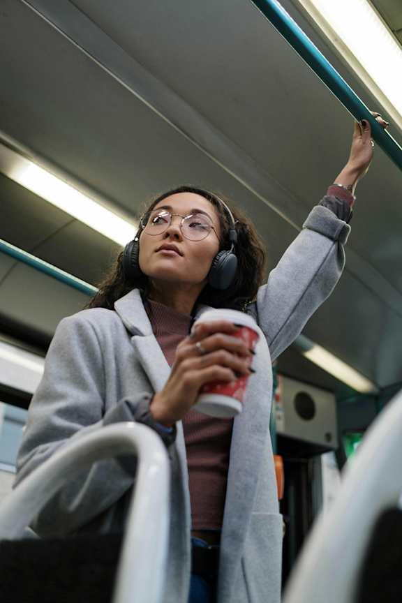 A woman in a grey coat is holding a red cup while standing in a subway car.