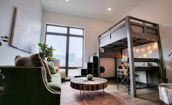 A room with a green couch, a wooden coffee table, and a bunk bed.