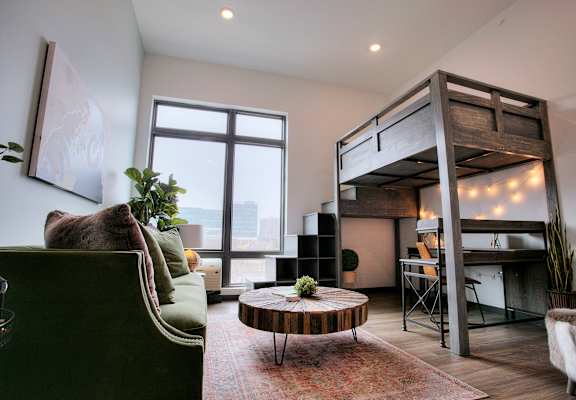 A room with a green couch, a wooden coffee table, and a bunk bed.