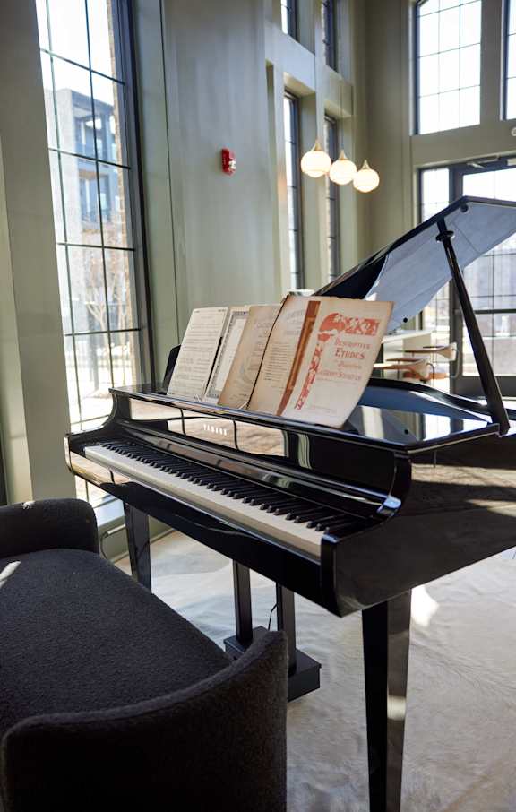 A grand piano with sheet music on top is placed in a room with large windows.