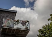 Thumbnail 2 of 7 - a house with flowers on the balcony and clouds in the sky