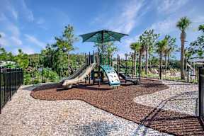 A playground with a green umbrella and a slide.