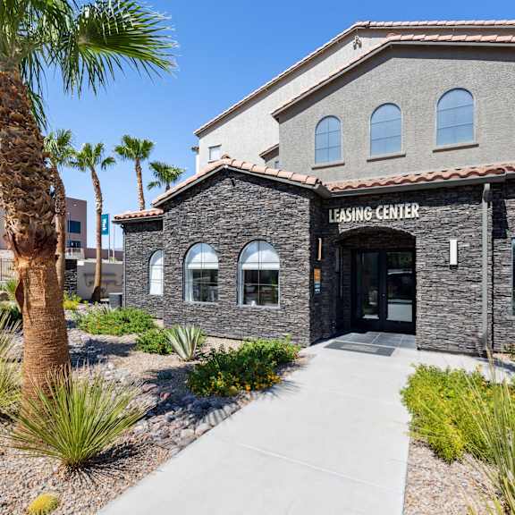 A building with a stone facade and a sign that reads "Leasing Center" is surrounded by palm trees and landscaping.