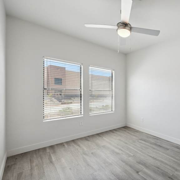 A room with a ceiling fan and two windows.