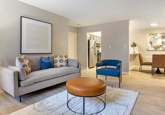 A living room with a beige couch, a blue chair, and a brown ottoman.
