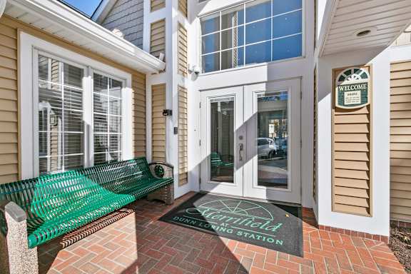 A green bench sits outside a building with a sign that says "Welcome".