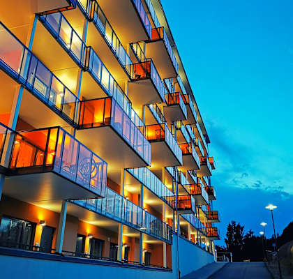 A modern building with balconies is illuminated by warm lighting.