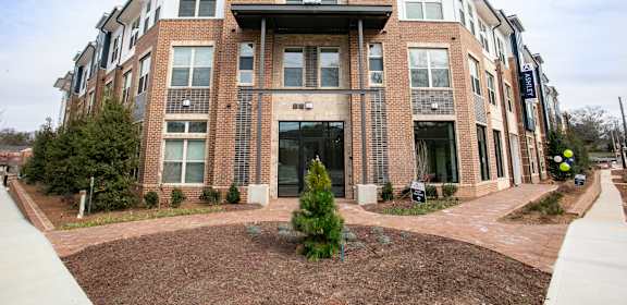 A large brick building with a black awning and a small tree in front.
