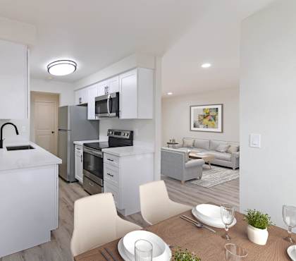 A modern kitchen with white cabinets and appliances, a dining table set with plates and glasses, and a couch in the background.