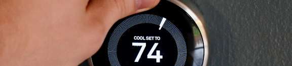 A person is adjusting a thermostat set to 74 degrees.