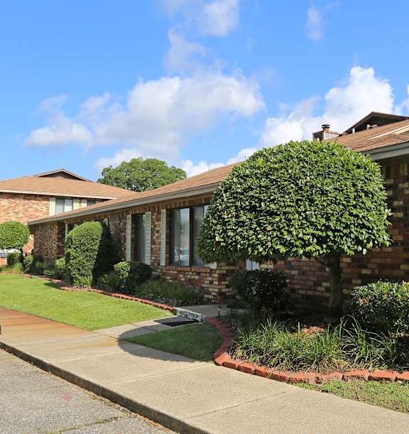 A house with a red brick wall and a green bush in front.