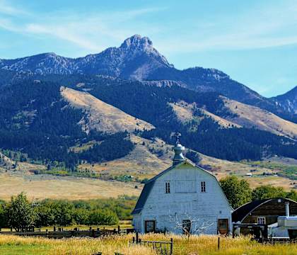 A white barn sits in front of a mountain range.
