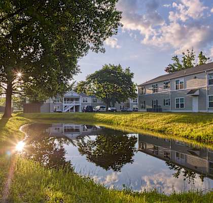 a small pond in the middle of a grassy area with a building in the background