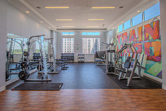 A gym with a variety of equipment and a large painting on the wall.