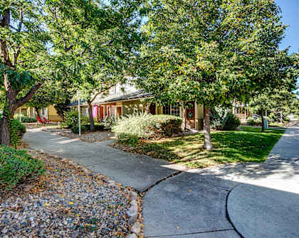 a sidewalk in front of a yellow house with trees
