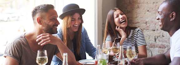 a group of people sitting at a table laughing and drinking wine