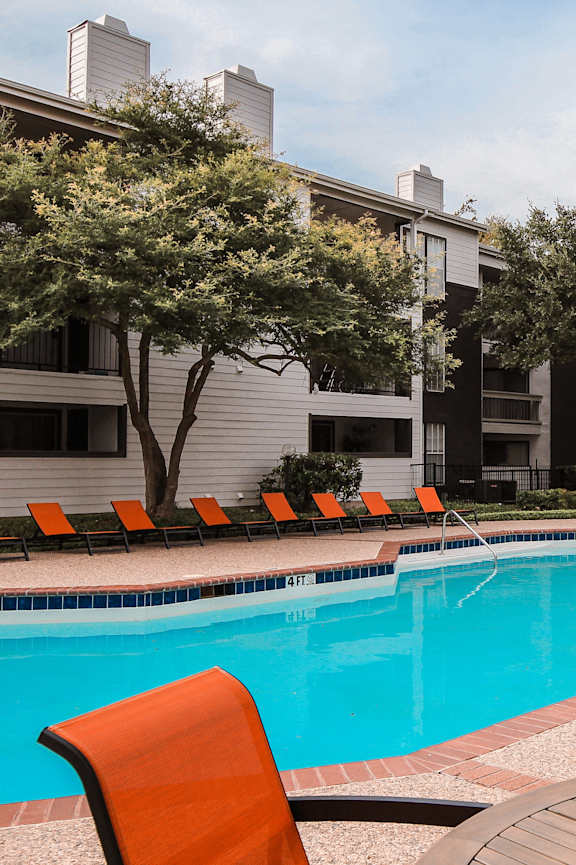 a swimming pool with orange chairs and a building in the background