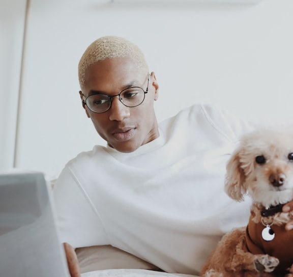 a man sitting in bed with a dog looking at a laptop computer